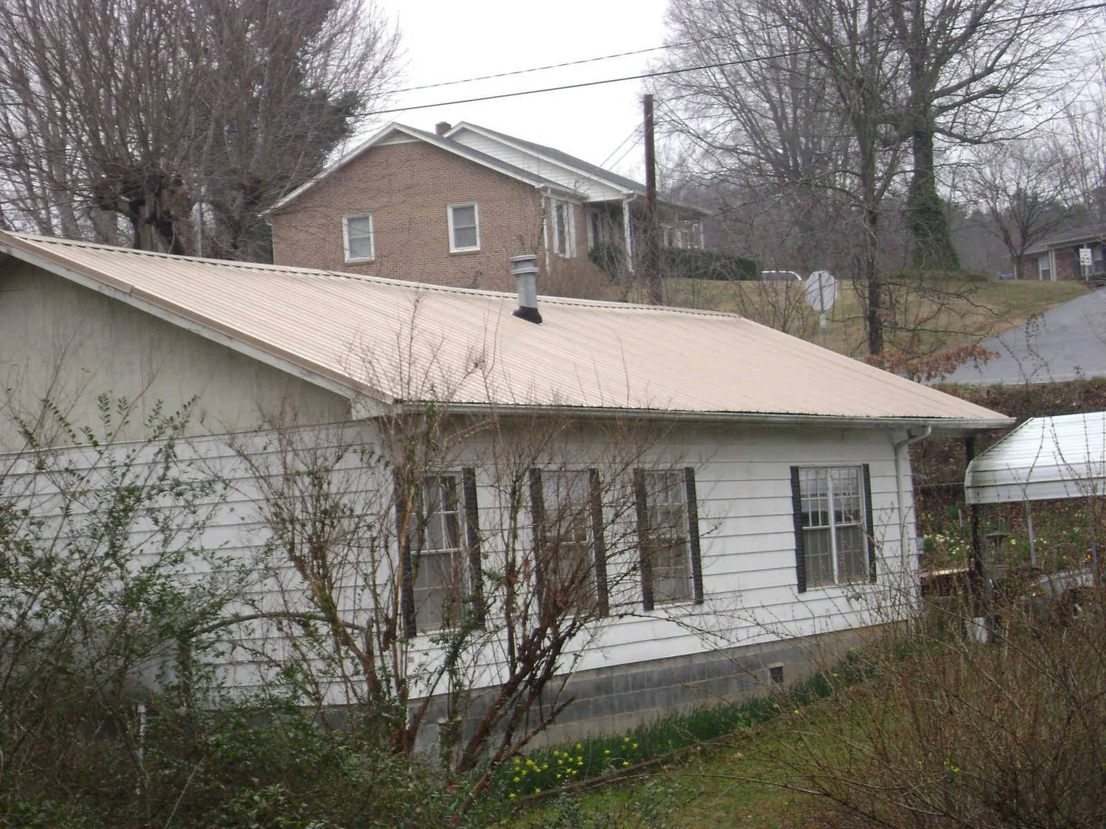 Tan metal roof on a white sided house set into a hillside — Commercial Roofing by Roofing Brothers in Moody