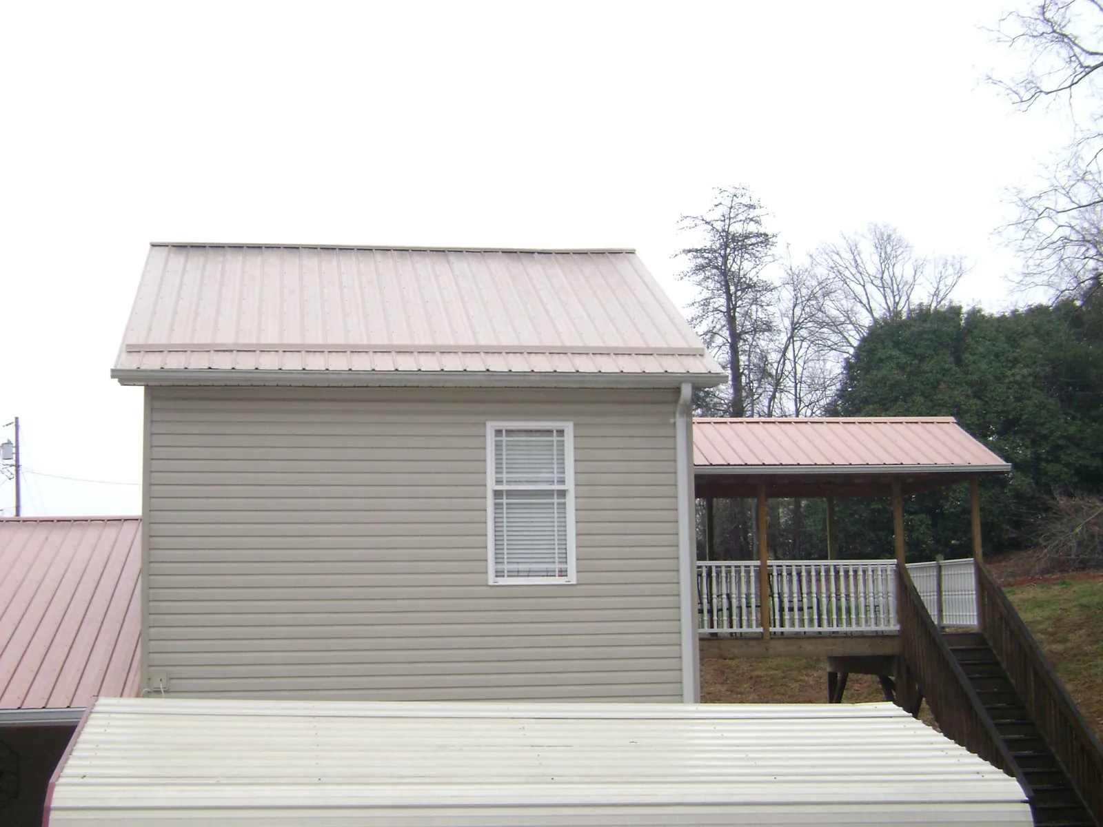 Tan metal roofs on a two story addition and attached porch, from a Roof Replacement job in Moody